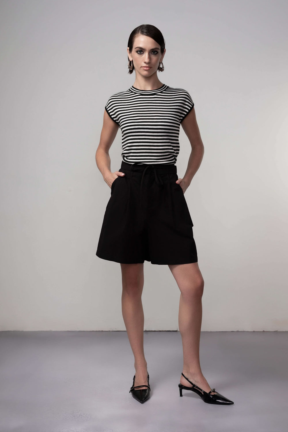 Femme portant un Bermuda coupe fluide noir, parfait pour une tenue estivale élégante, associé à un t-shirt rayé pour un look moderne.