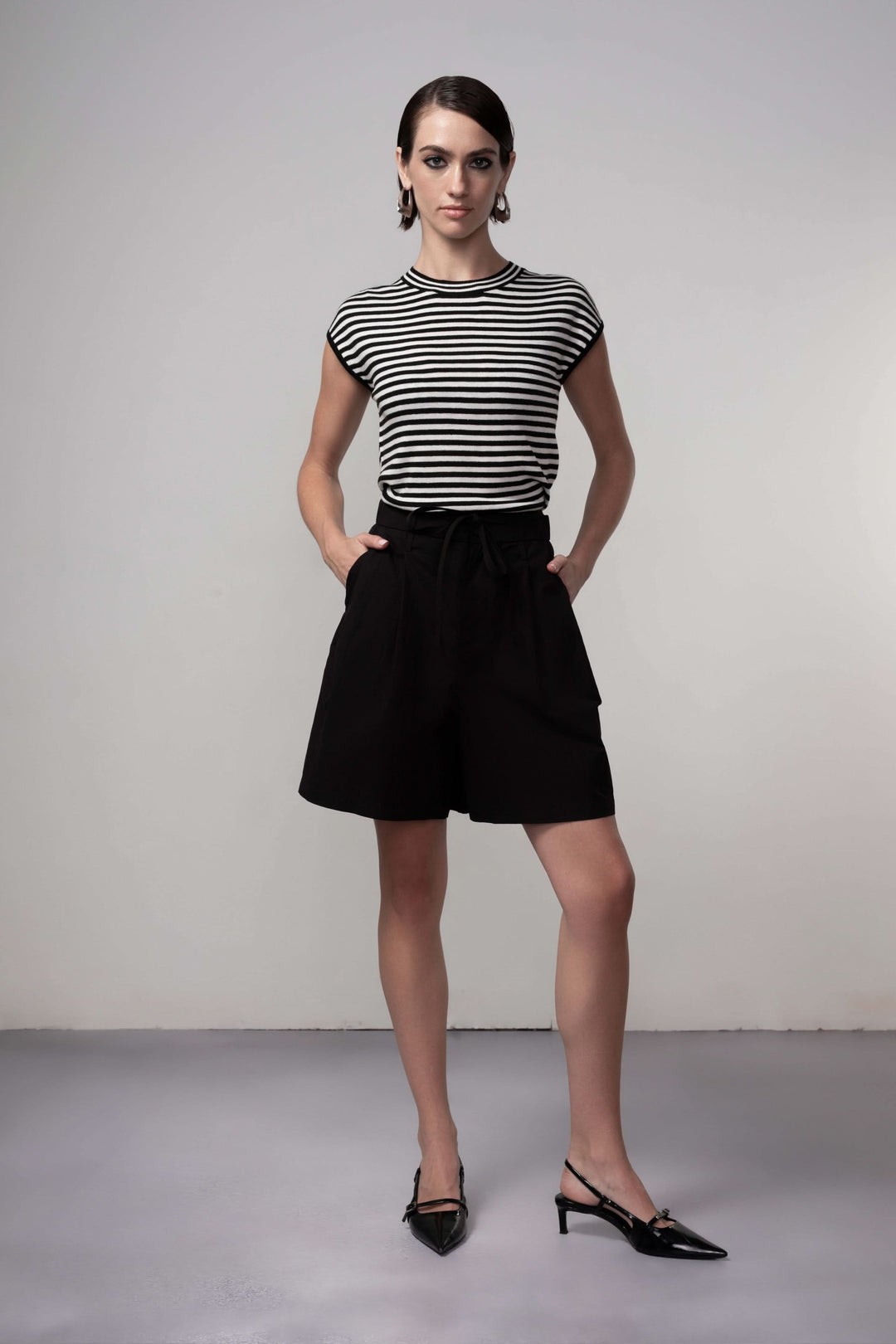 Femme portant un Bermuda coupe fluide noir, parfait pour une tenue estivale élégante, associé à un t-shirt rayé pour un look moderne.