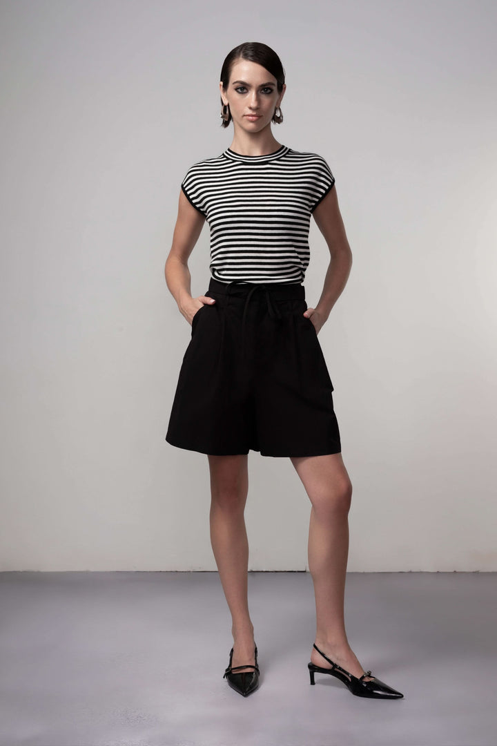 Femme portant un Bermuda coupe fluide noir, parfait pour une tenue estivale élégante, associé à un t-shirt rayé pour un look moderne.