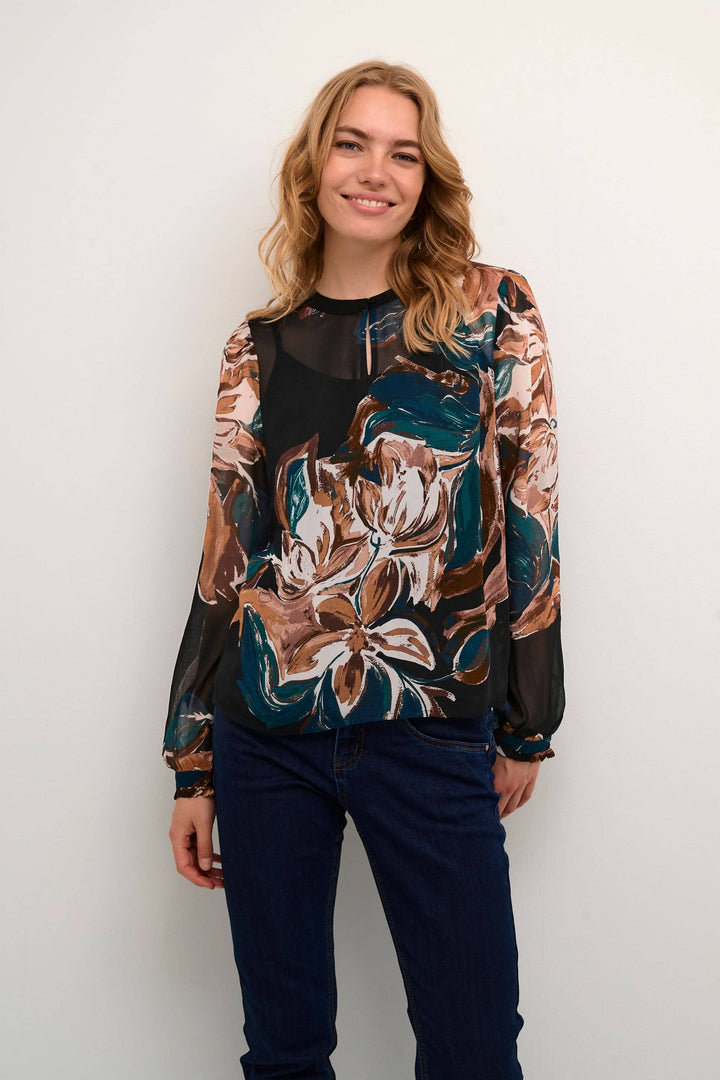 Blouse Jasmina avec imprimé floral, légère transparence et manches longues, portée par un modèle souriant.