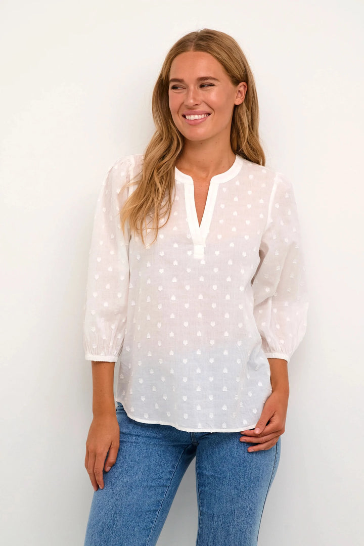 Blouse Jollia à manches bouffantes en coton blanc, encolure en V, portée avec un jean, chic et décontractée.