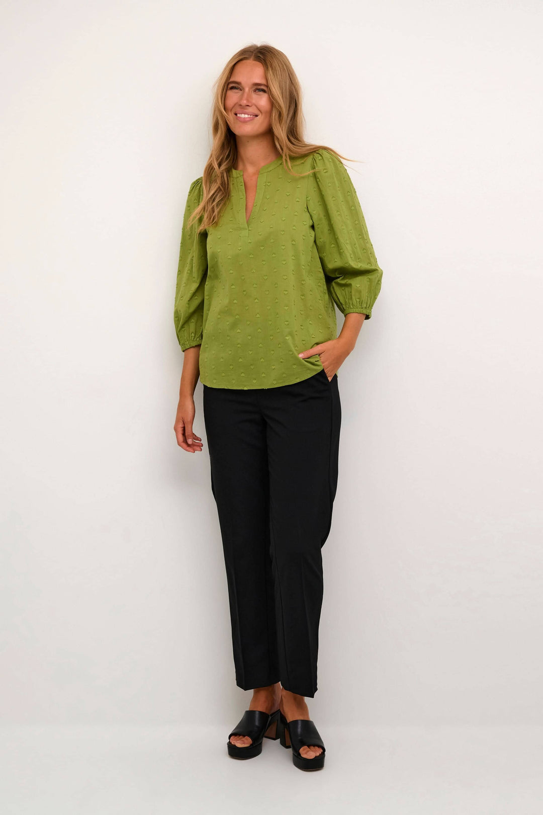 Modèle portant une blouse à manches 3/4 verte et un pantalon noir, style décontracté et élégant.