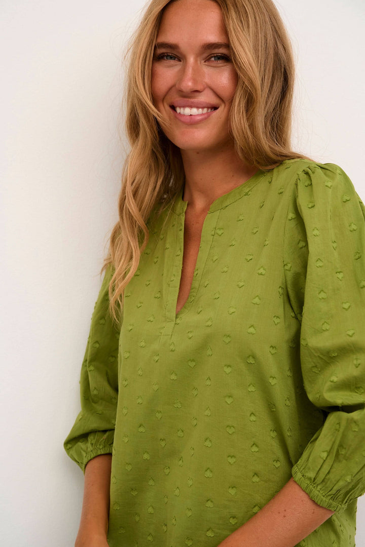 Blouse Jollia verte avec manches 3/4 et détails en forme de cœur, idéale pour un style décontracté et élégant.