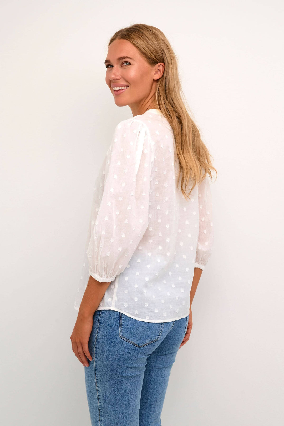 Femme souriante portant une blouse blanche à manches bouffantes avec des détails de couture en forme de cœur.