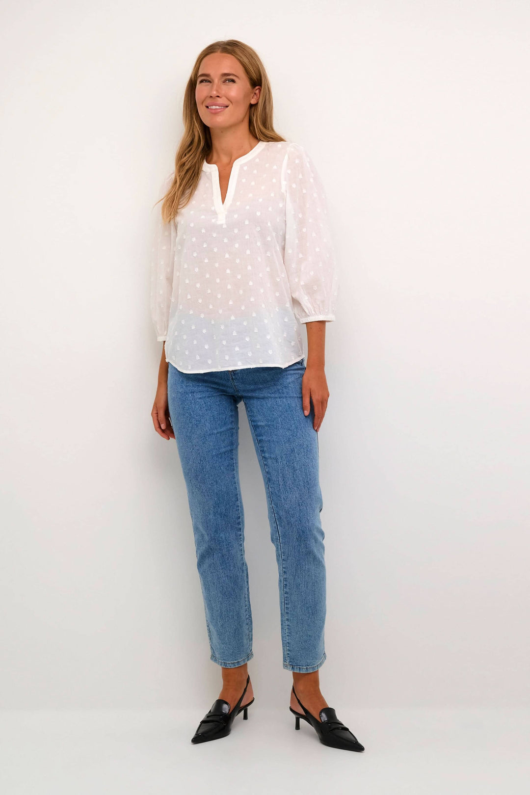 Blouse Jollia à manches 3/4, en coton blanc, avec encolure en V et détail de couture en cœur, portée avec un jean.