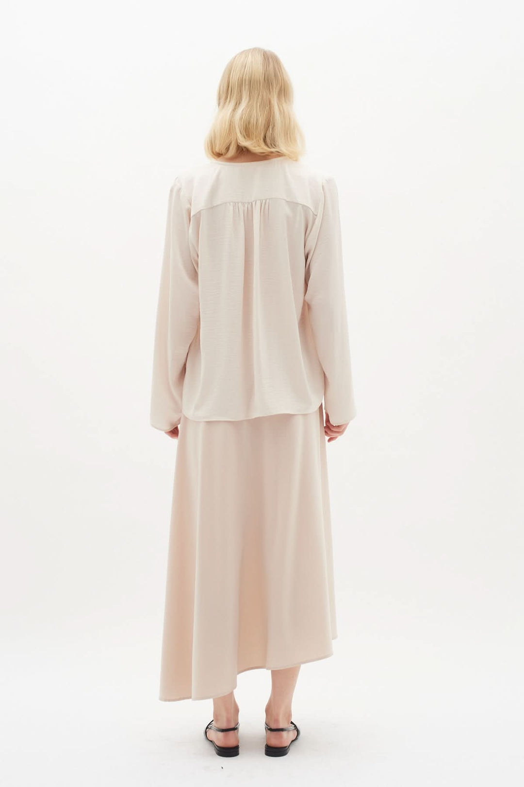 Blouse Mato, chemise classique à manches longues, encolure nouée, portée avec une jupe légère, couleur beige.