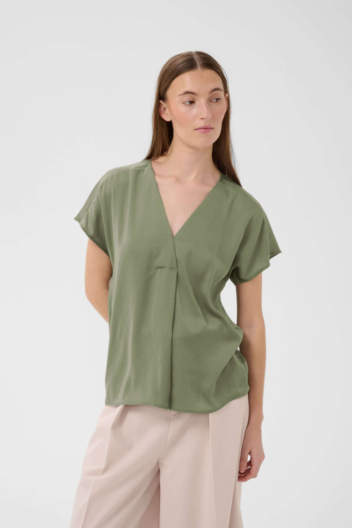 Femme portant une Blouse Rinda vert olive avec encolure en V et coupe droite, mettant en valeur sa silhouette élégante.