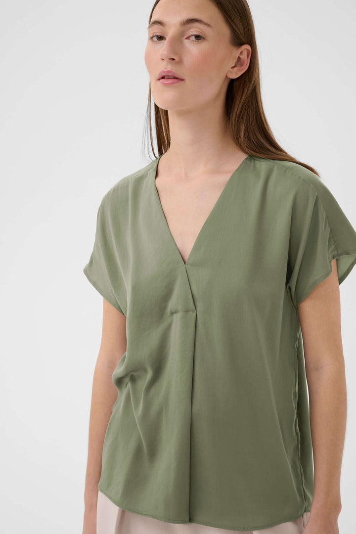 Femme portant la Blouse Rinda en tissu fluide vert avec encolure en V et coupe droite élégante, idéale pour un style épuré et féminin.