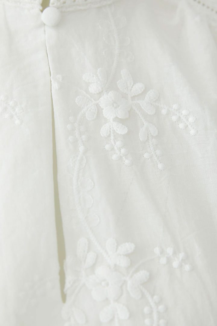 Blouse à broderies florales avec détail de broderie florale raffinée sur tissu blanc.