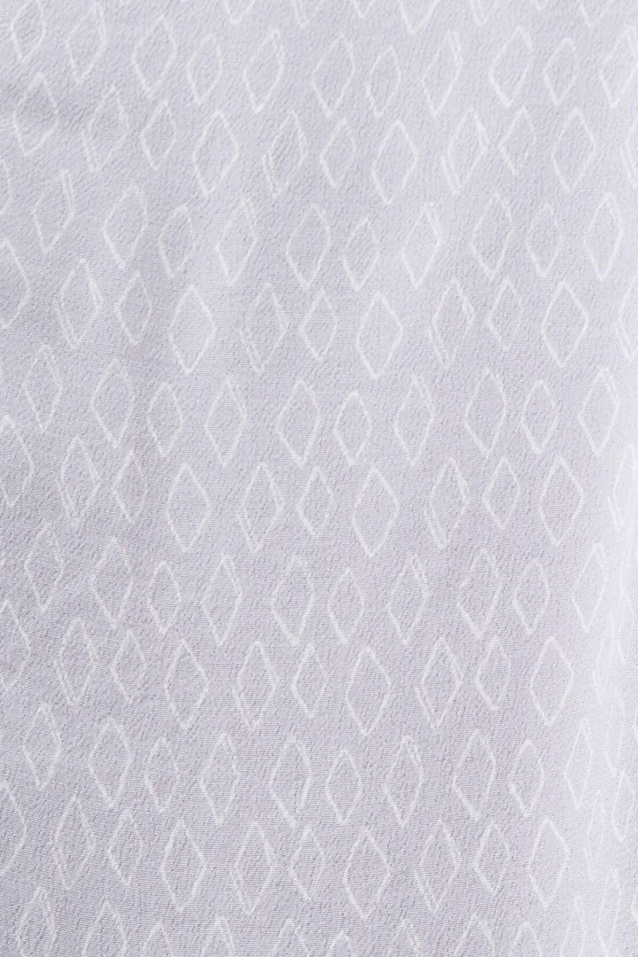 Tissu crêpe texturé blanc avec motif géométrique en losanges, utilisé pour un blouse col V.