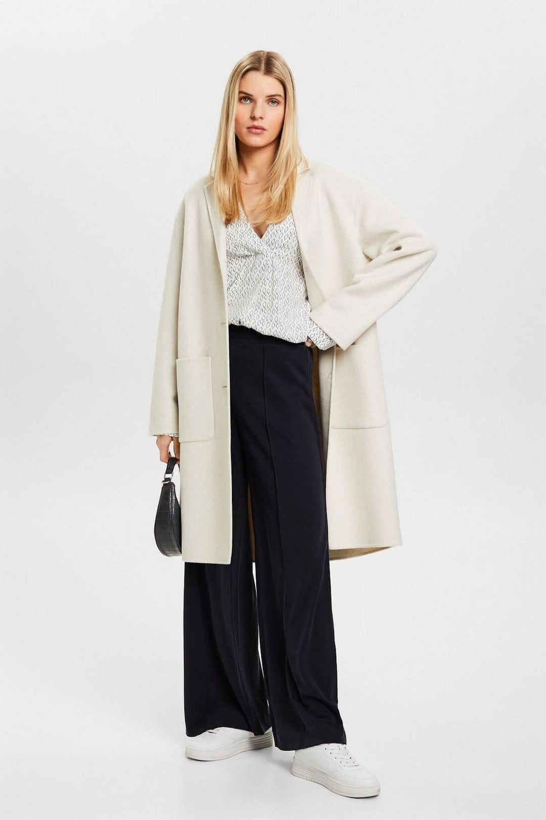Femme en blouse col V et pantalon ample, portant un manteau beige, tenue décontractée et élégante.