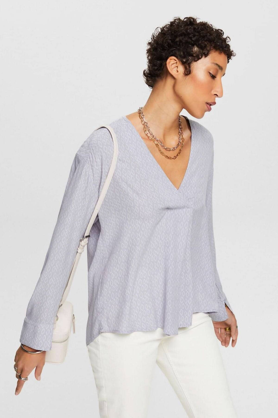 Blouse col V en tissu crêpe texturé, coupe ample, manches tombantes, portée avec un sac élégant.