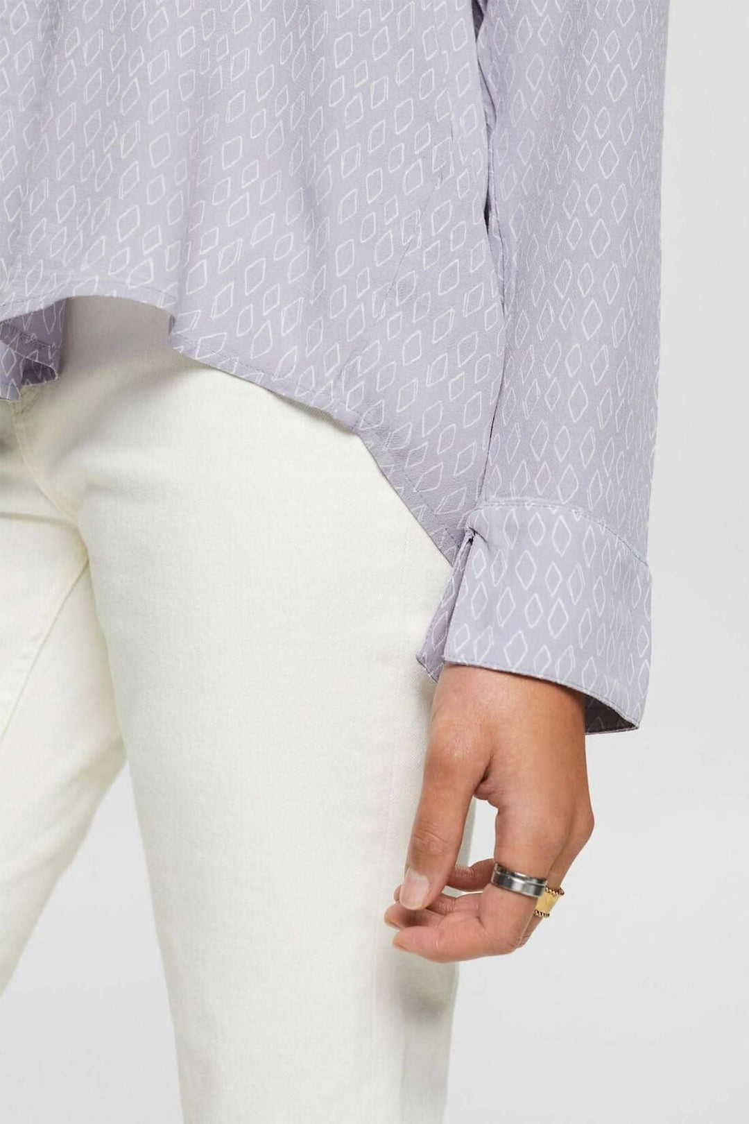 Chemisier col V en crêpe texturé, coupe ample, manche avec poignets fendus, porté avec un pantalon blanc.