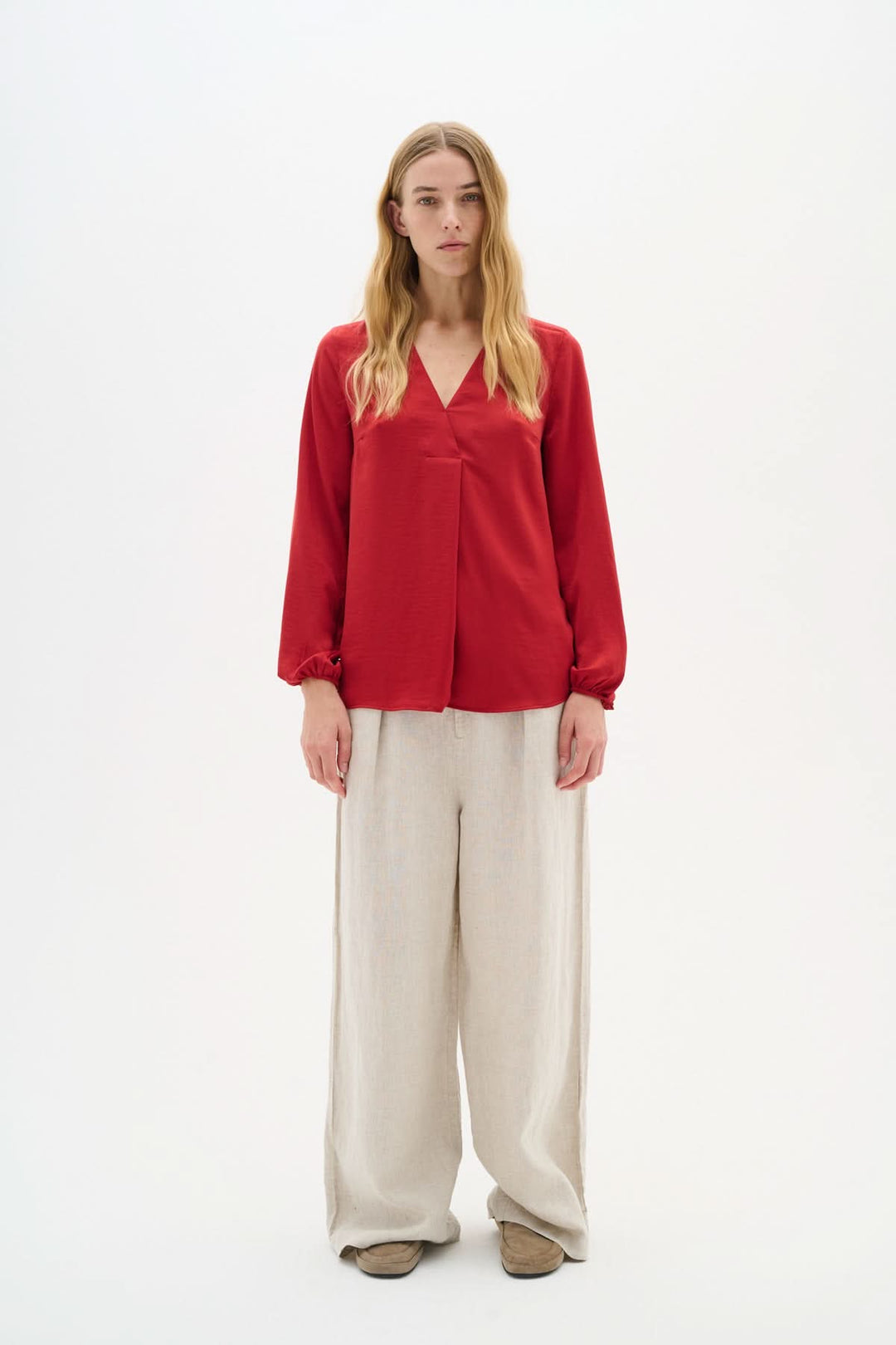 Blouse col en V Rinda rouge avec manches longues, associée à un pantalon beige pour un look moderne et élégant.
