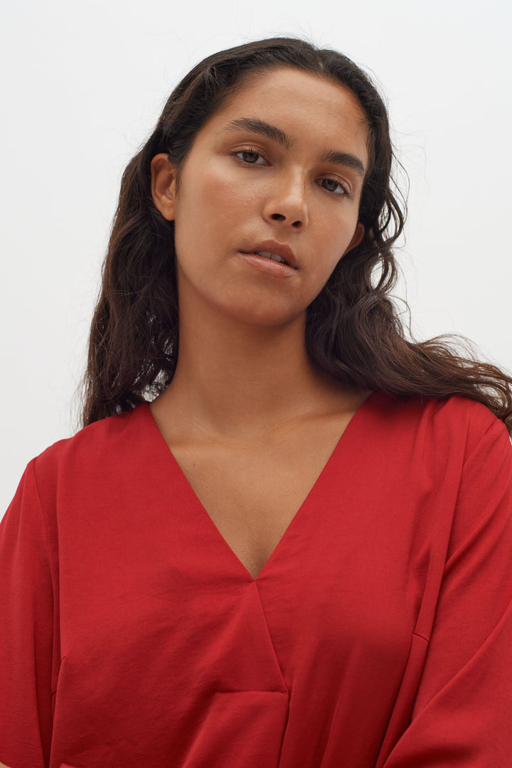 Blouse col en V Rinda rouge avec manches longues, tenue moderne et élégante.