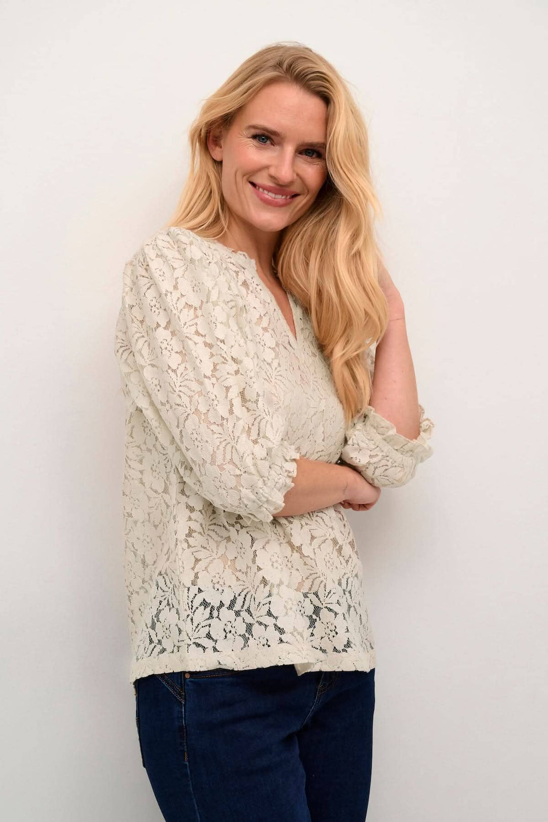 Blouse en dentelle blanche avec manches retroussées, style décontracté, portée par une femme souriante.