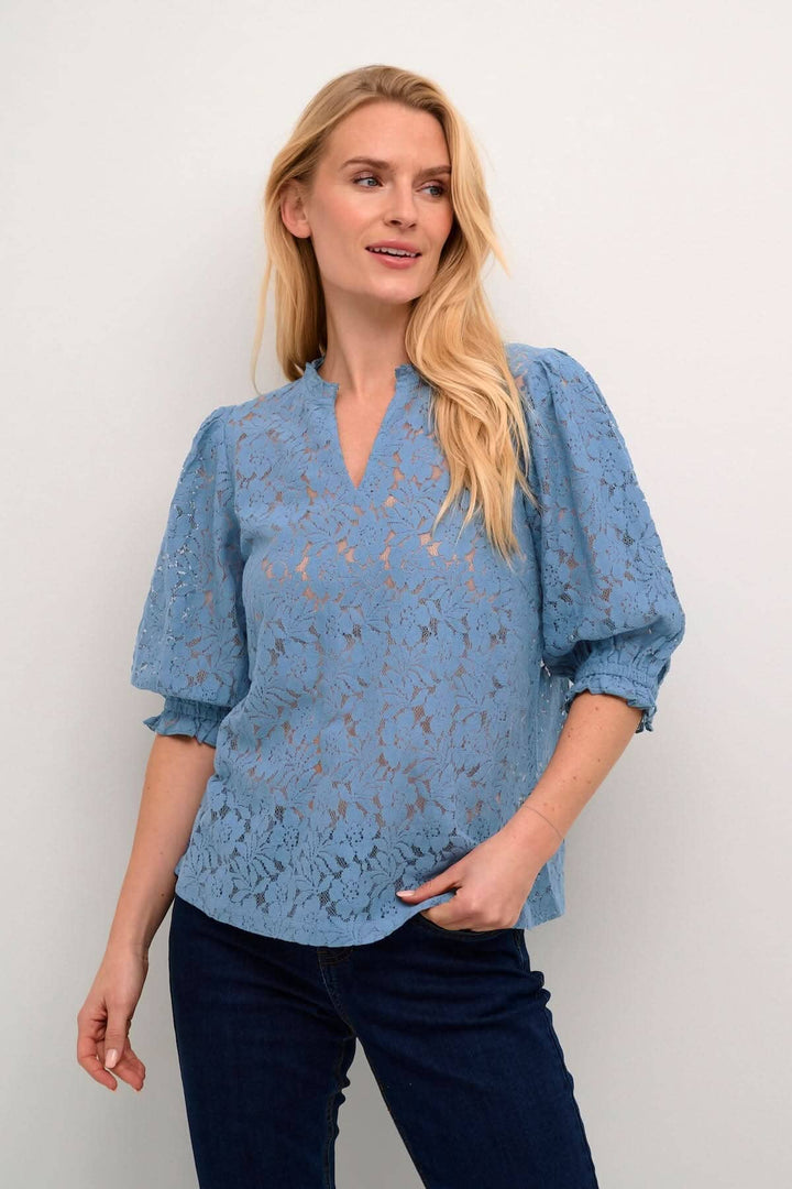 Blouse de Kaspis en dentelle bleue avec manches bouffantes, élégante et décontractée, idéale pour le travail ou les sorties.