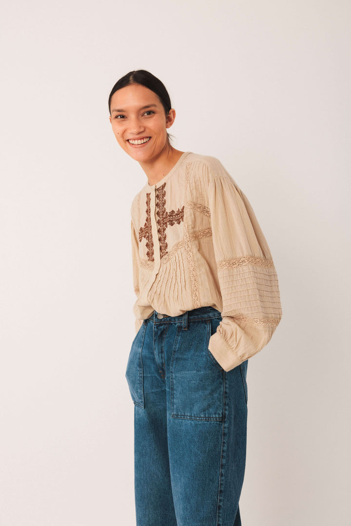 Femme portant une blouse ethnique brodée beige à manches longues bouffantes, avec un jean taille haute pour un look bohème chic.