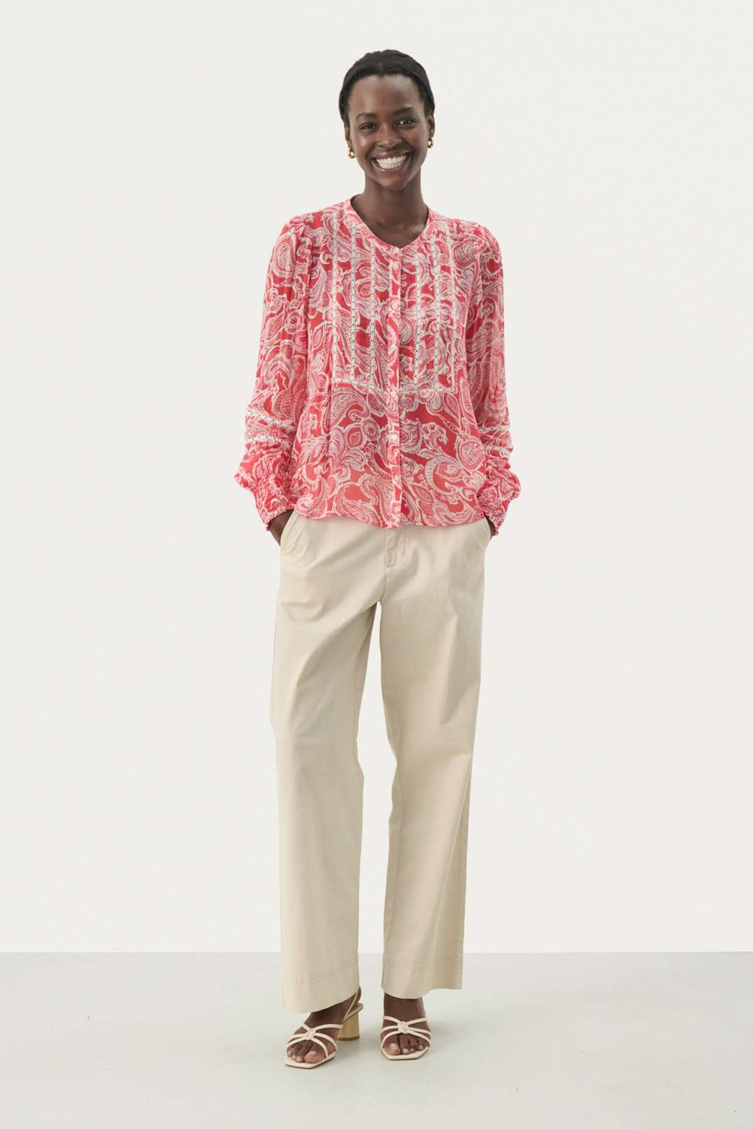 Blouse fluide Nesma à micro-motif fleuri, manches longues, portée avec un pantalon beige.