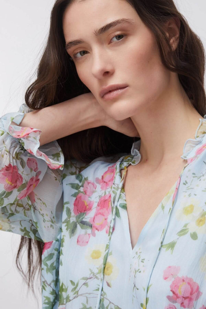 Blouse fluide à imprimé floral avec encolure en V et manches longues, portée par une femme, reflétant une allure féminine et romantique.