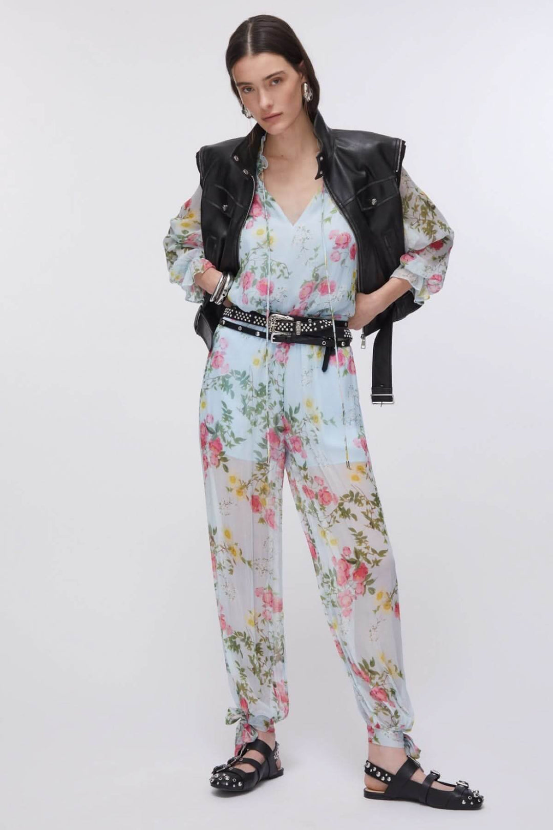 Femme portant une blouse fluide à imprimé floral avec veste en cuir et sandales noires.