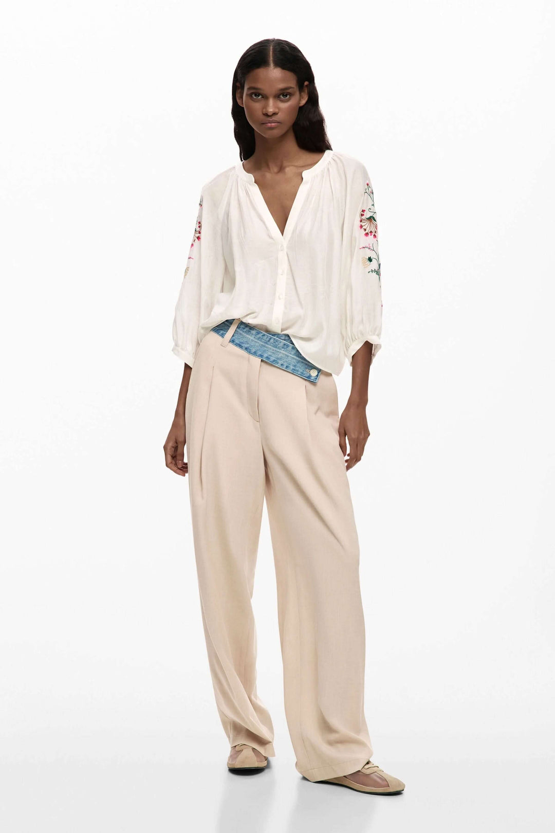 Modèle portant une blouse fluide à manches brodées avec un pantalon beige