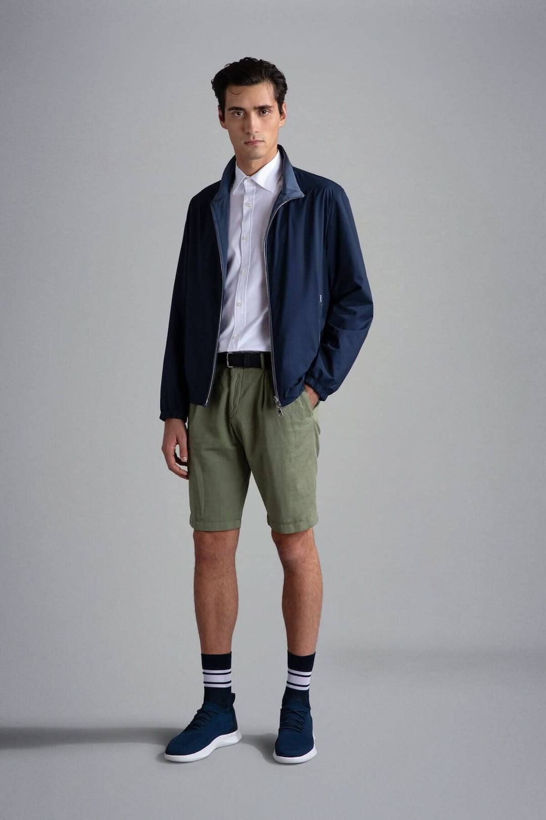Homme portant un blouson imperméable réversible, chemise blanche et shorts kaki, look décontracté et moderne.