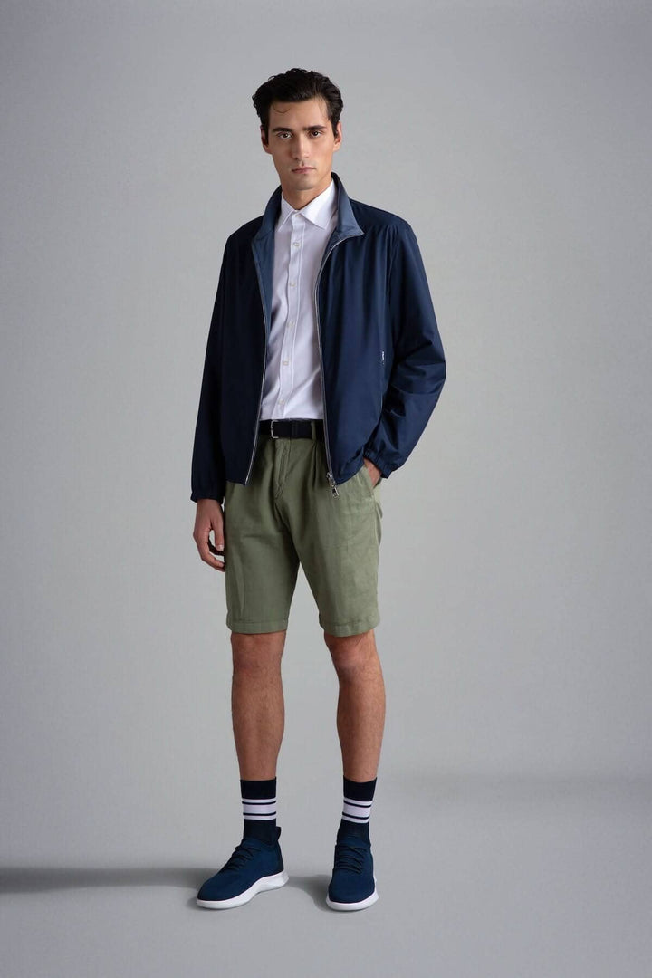 Homme portant un blouson imperméable réversible, chemise blanche et shorts kaki, look décontracté et moderne.