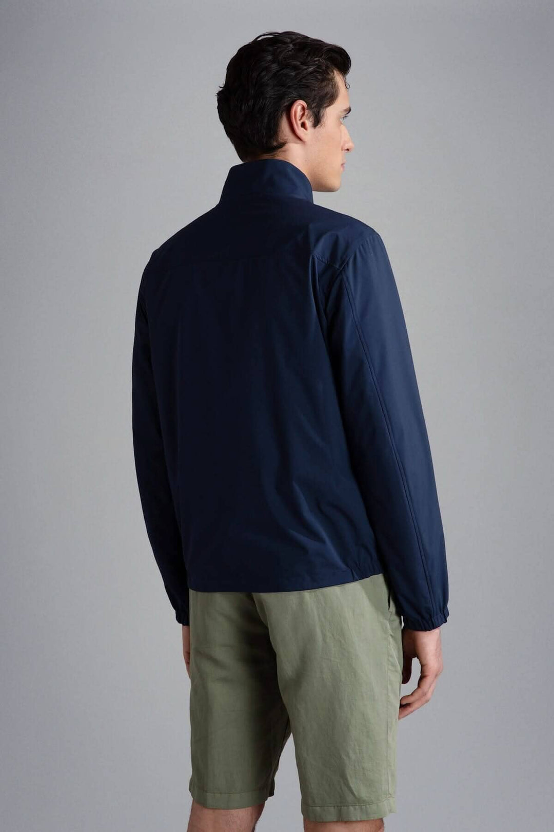 Homme portant un blouson imperméable réversible navy vu de dos, associé à un short beige.