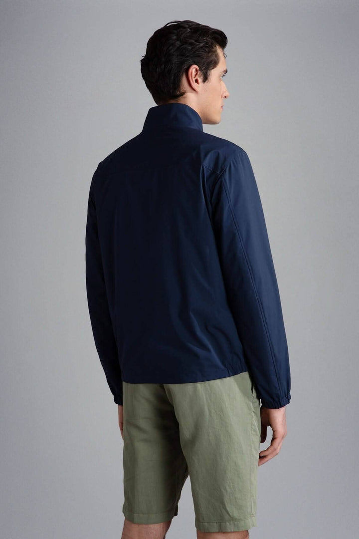 Homme portant un blouson imperméable réversible navy vu de dos, associé à un short beige.