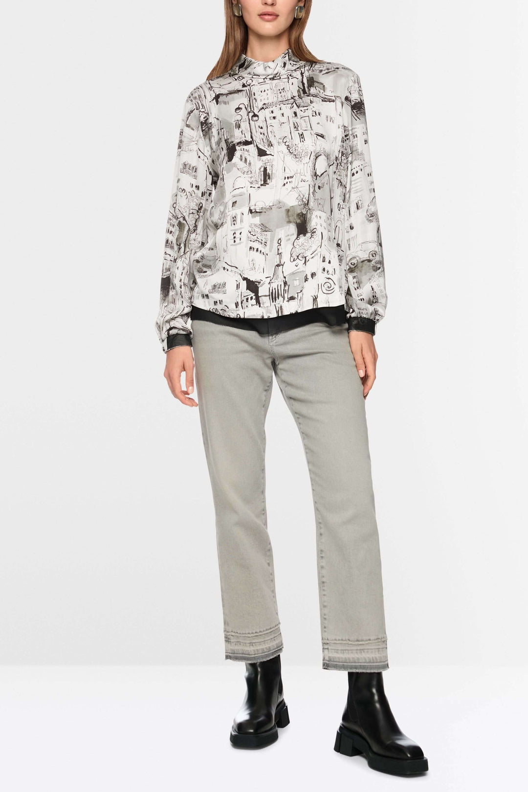 Blouse à imprimé CITY au motif artistique urbain avec manches longues et col montant, assortie à un pantalon sobre et des bottes noires.
