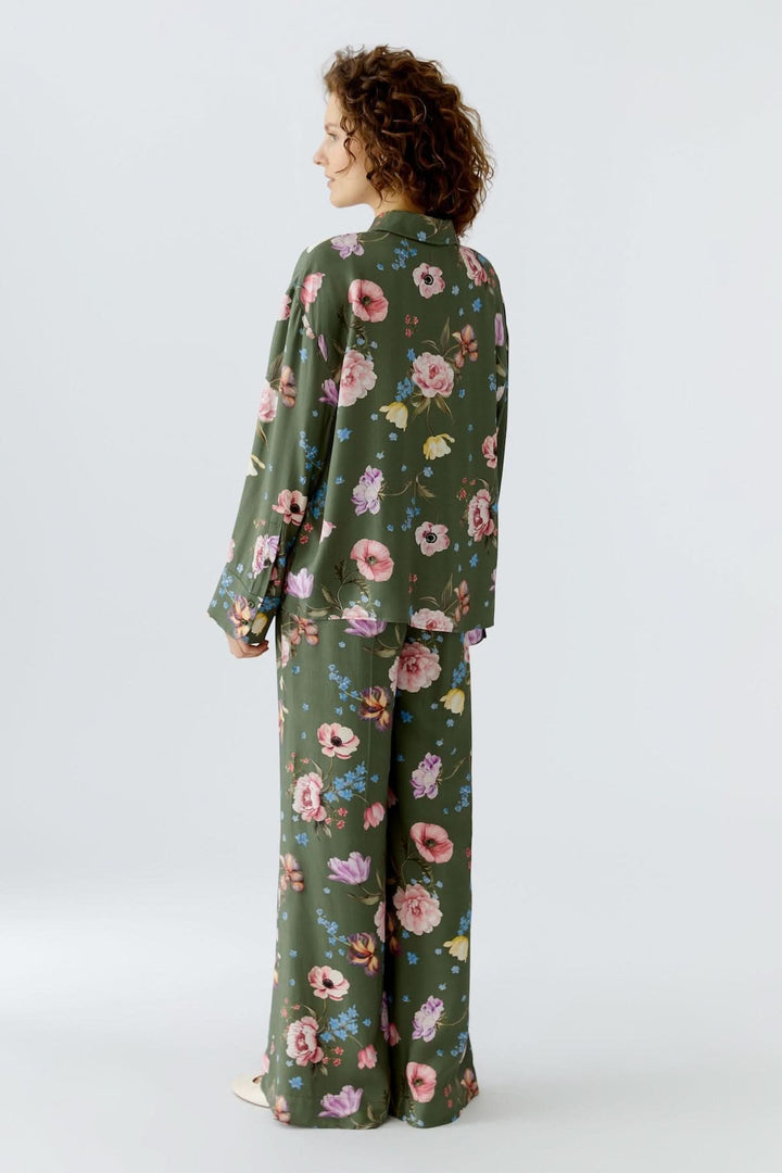 Femme portant une blouse à imprimé floral fluide avec manches longues et col chemise classique, design féminin et moderne.
