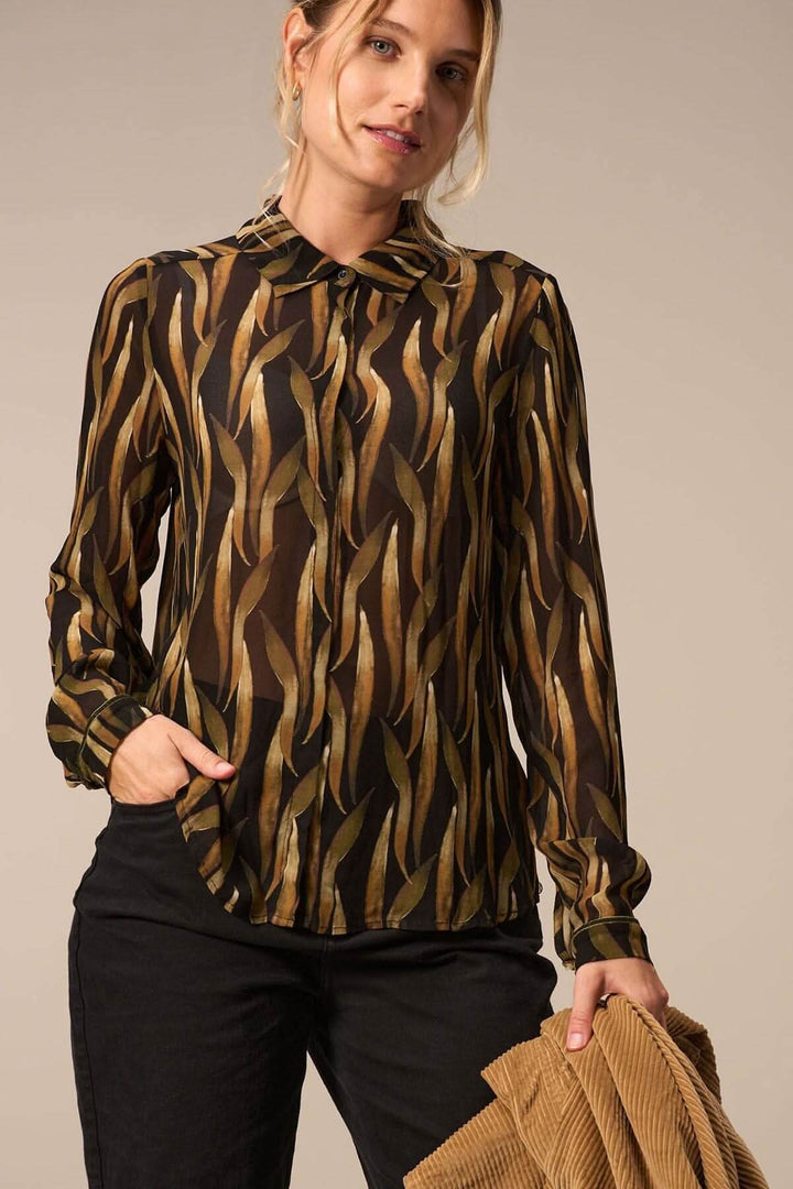 Blouse imprimée à motifs végétaux, manches longues, look élégant et transparent, portée avec un pantalon noir.