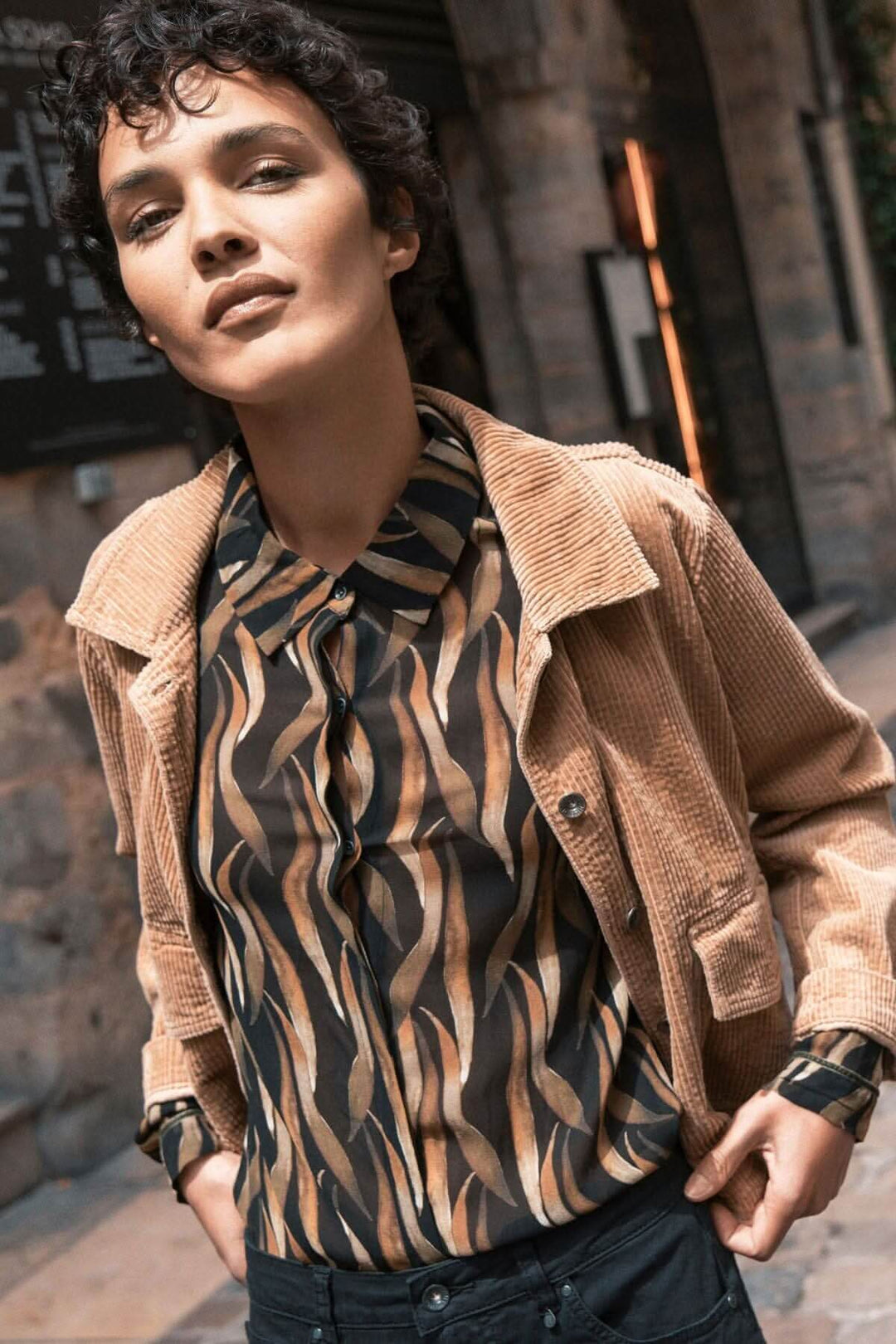 Femme portant une blouse imprimée à motifs végétaux et une veste en velours côtelé, look urbain élégant.