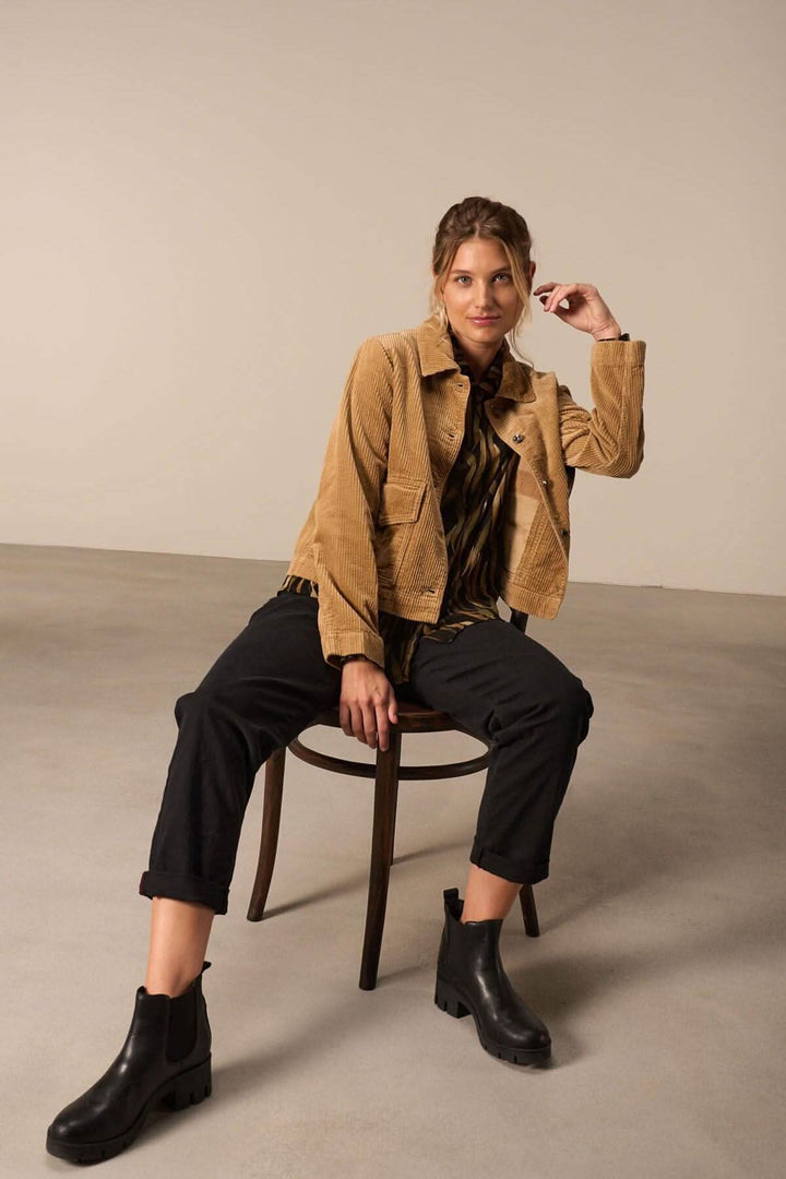 Femme assise sur une chaise en tenue décontractée avec une veste en velours et des bottines noires.