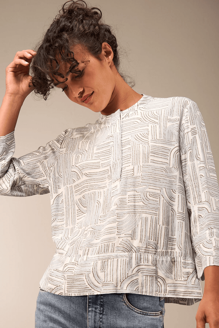 Femme portant une Blouse à manches 3/4 avec encolure ronde et motif graphique, apportant une allure moderne et élégante.