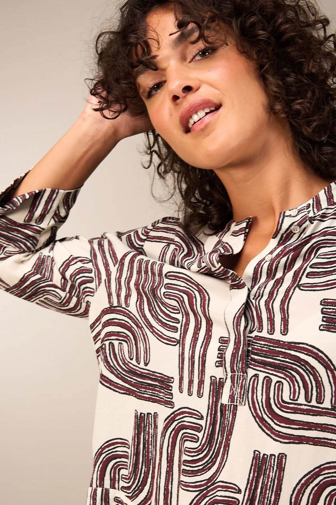Femme portant une blouse à manches 3/4 à motifs, encolure ronde et patte boutonnée, style moderne et élégant.