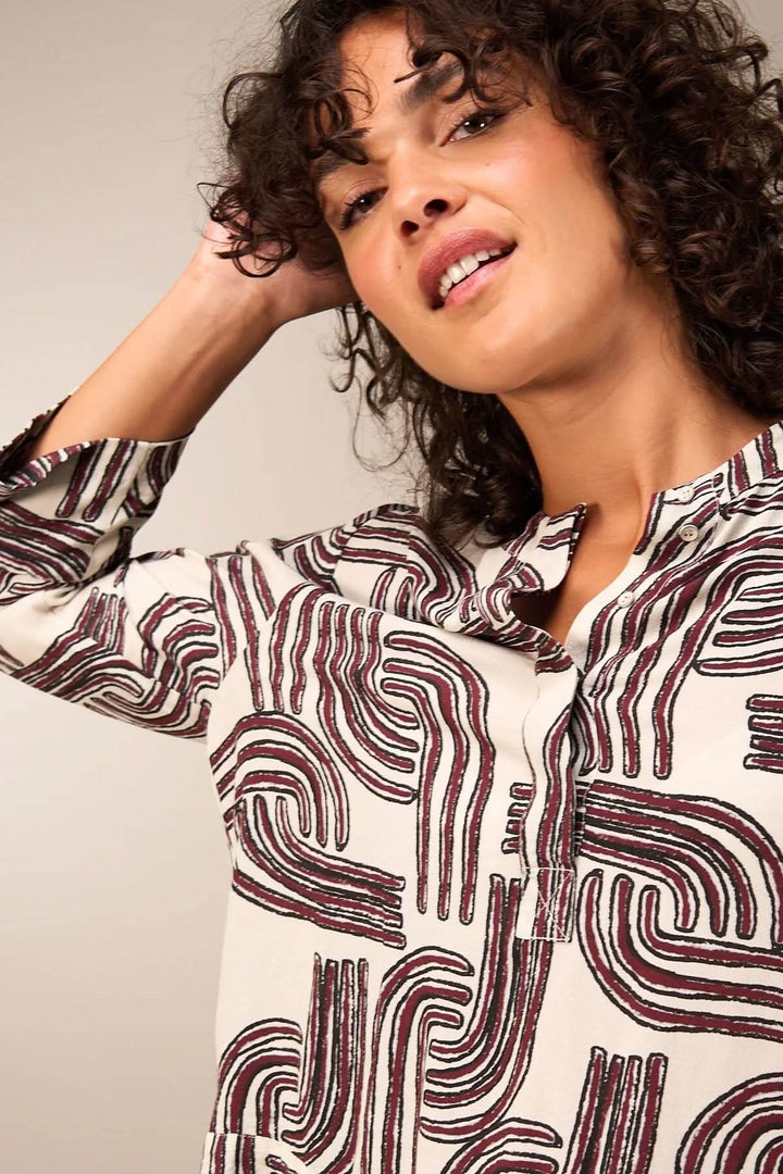 Femme portant une blouse à manches 3/4 à motifs, encolure ronde et patte boutonnée, style moderne et élégant.