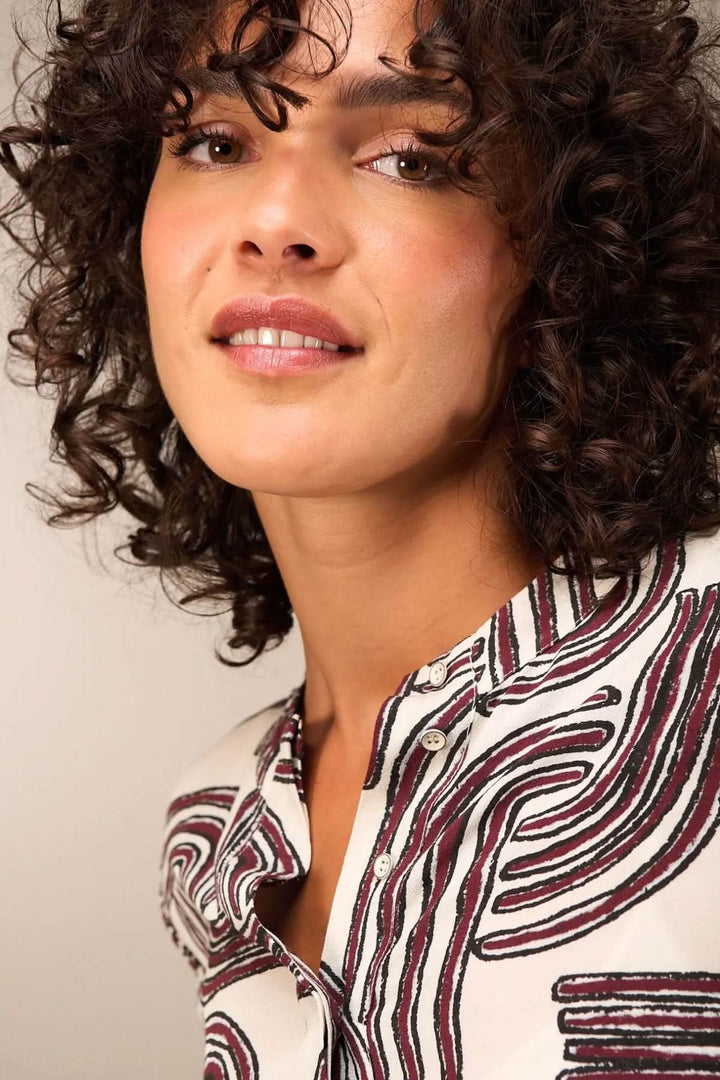 Femme portant une blouse à manches 3/4 avec encolure ronde et patte boutonnée, tissu fluide et motif moderne.