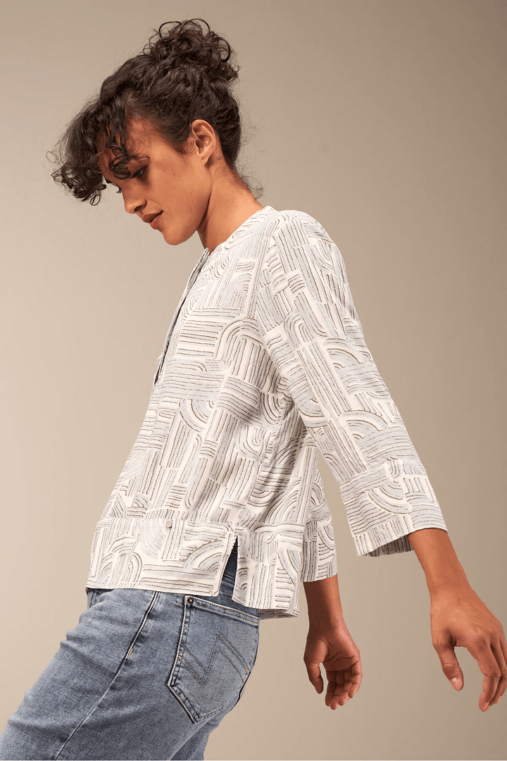Blouse à manches 3/4 en tissu fluide avec encolure ronde et patte boutonnée, portée avec un jean pour un look moderne.