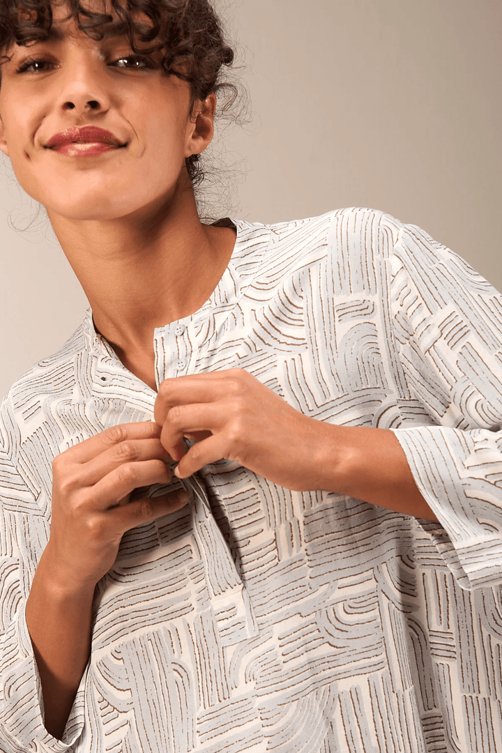Femme portant une blouse à manches 3/4 en tissu fluide avec encolure ronde, idéale pour un style moderne et confortable au quotidien.