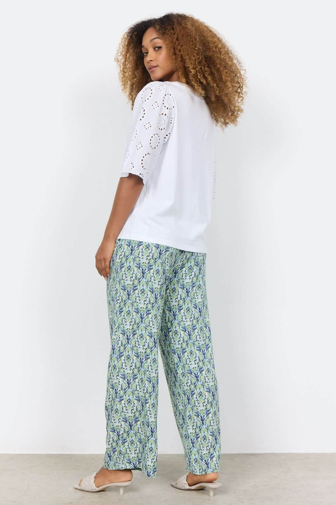 Blouse blanche à manches brodées, portée avec un pantalon à motif, vue de dos, style décontracté.