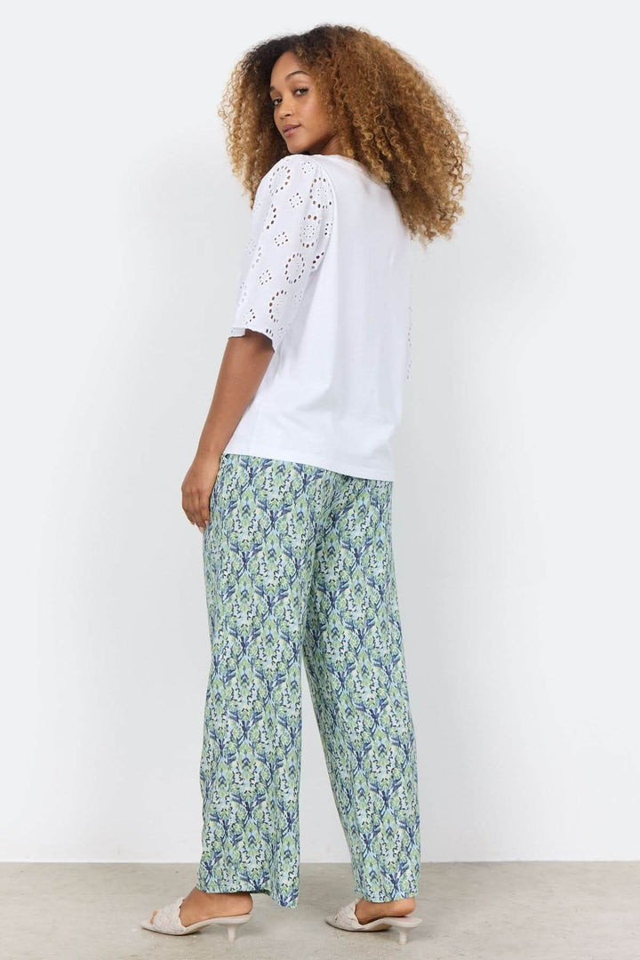 Blouse blanche à manches brodées, portée avec un pantalon à motif, vue de dos, style décontracté.