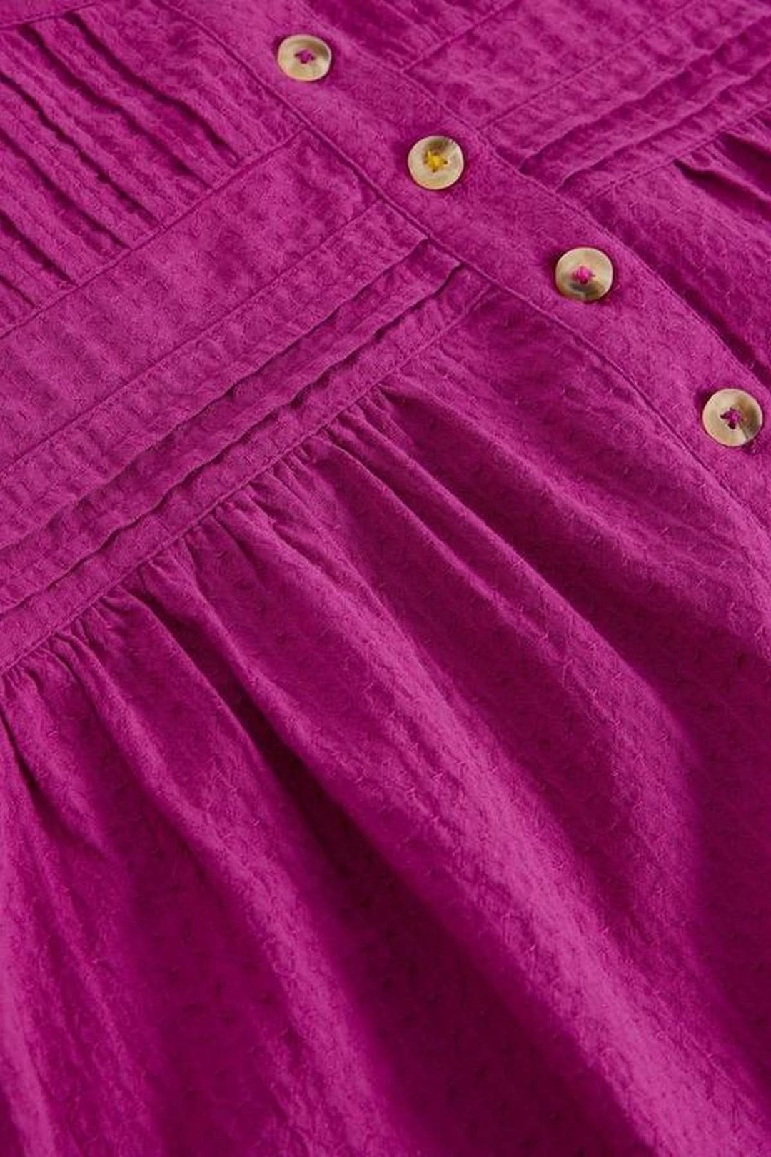 Détail en gros plan de la blouse plumetis à plastron froncé avec texture et boutons.