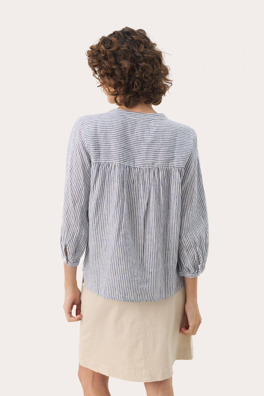 Femme vue de dos portant une blouse à rayures bleues en lin, avec manches trois quarts et col rond.