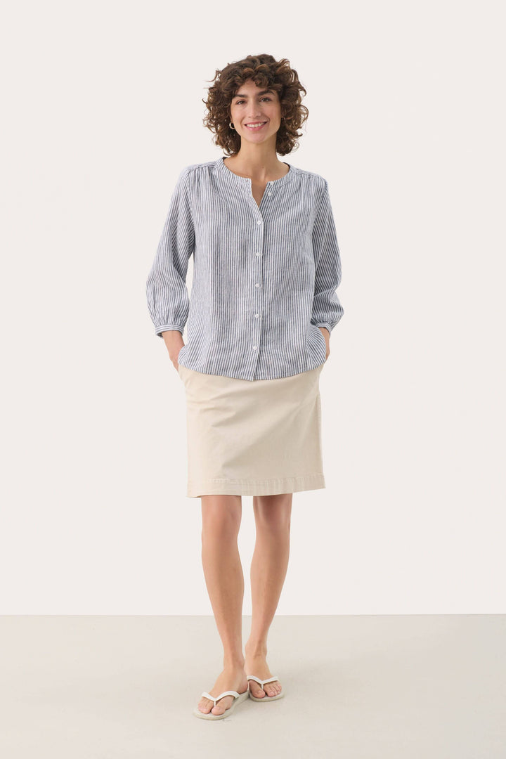 Femme portant une blouse à rayures en lin, manches trois quarts, et jupe beige, style décontracté et élégant.