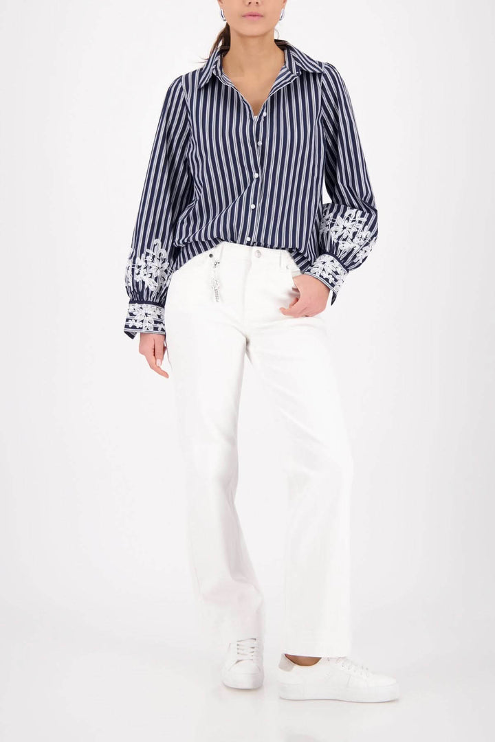 Blouse à rayures avec broderies florales aux poignets, élégante et intemporelle, portée avec un pantalon blanc et des baskets.
