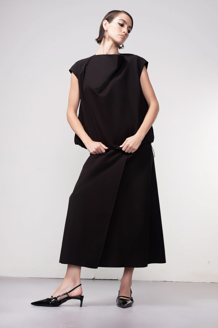 Femme portant une blouse sans manches avec design épuré et coupe fluide, illustrant élégance et modernité.