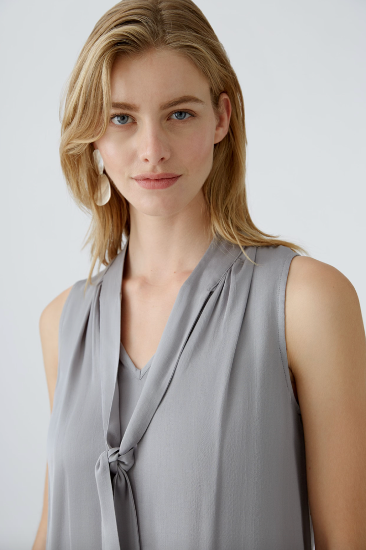 Blouse en satin brillant avec cravate, encolure en V et coupe décontractée, portée par modèle blonde.