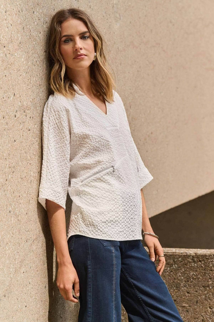 Femme portant une blouse gaufrée à col V et manches courtes, avec poches zippées.